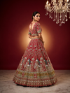 Back profile of a bride wearing a heavily embroidered red silk blouse with intricate thread work and stones.

