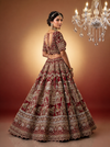 Back view of a bride in a heavily embroidered cherry red blouse and silk lehenga with gold zari work.
