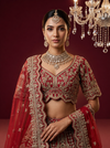 Close-up of royal procession embroidery with camel riders and architectural details on a red silk bridal lehenga.