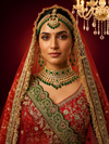 Close-up portrait of a bride in a Red Silk Lehenga with heavy gold zari and green emerald jewelry.
