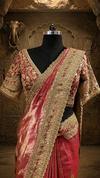 Full-length front view of a model styling a shimmering rust tissue saree with an ornate gold zari border under a luxury crystal chandelier.
