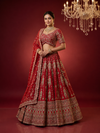 Full-length front view of a model in a red bridal lehenga with a matching dupatta and heavy gold jewelry under a chandelier.