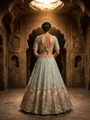 Full back profile of the sky blue lehenga outfit, highlighting the structured drape of the metallic silk skirt and the elegant sheer back of the choli.