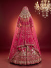 Full back view of a bride wearing a pink bridal lehenga with a sheer dupatta and intricate embroidery, standing under a chandelier.