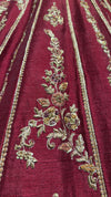 Close-up of maroon raw silk fabric featuring dense gold zardozi embroidery and delicate white pearl accents.