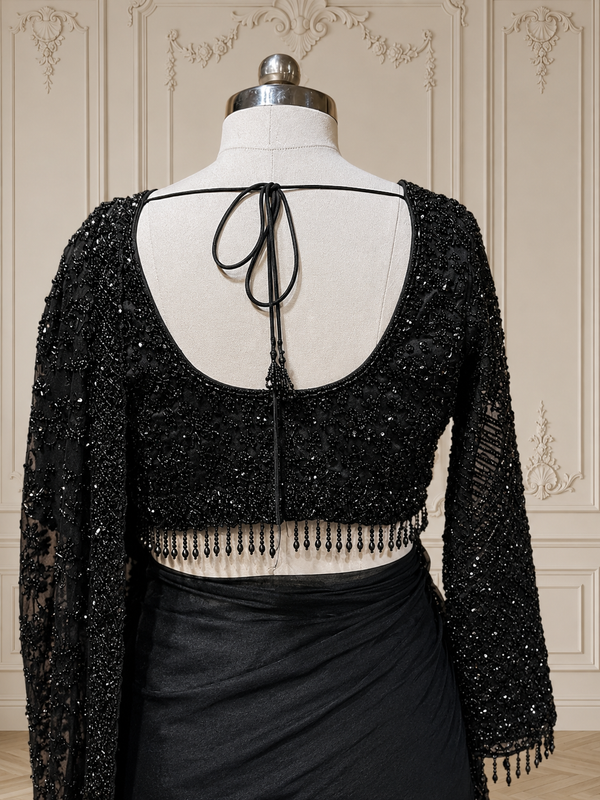 A front-facing medium shot highlighting the structured V-neckline of the matching black embroidered blouse and the rich texture of the pleated pallu neatly resting over the mannequin's shoulder.
