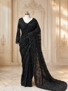 A grand full-length presentation of the midnight black net saree draped on a mannequin, showcasing the heavily detailed pallu trailing across a polished marble floor within a classic cream-colored European wall panel setting.