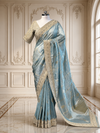 A majestic full-length display of the firozi tissue silk saree on a mannequin, highlighting its liquid metallic sheen, matching embroidered blouse, and the grand silver-gold scalloped borders trailing onto a luxury marble floor.
