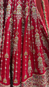 Macro shot of the red silk fabric highlighting the intricate manual work of sequins and cut beads on the lehenga's flares.